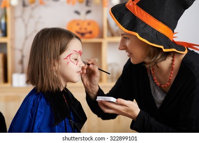 Woman Applying Halloween Make-up To Face Of Her Daughter