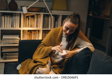 woman applying hand creme, sitting on sofa at home - Shutterstock ID 1981504691
