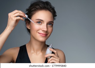 Woman Applying  Hyaluronic Serum On Her Face With Pipette. Photo Of Attractive Woman With Perfect Makeup On Gray Background. Beauty Concept