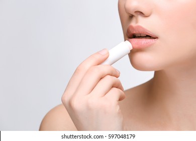 Woman applying hygienic lip balm on light background