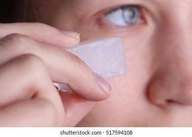 Woman applying ice cube to refresh her face skin near eyes. Beauty, skin care concept