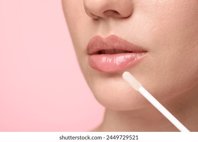 Woman applying lip gloss on pink background, closeup. Space for text - Powered by Shutterstock