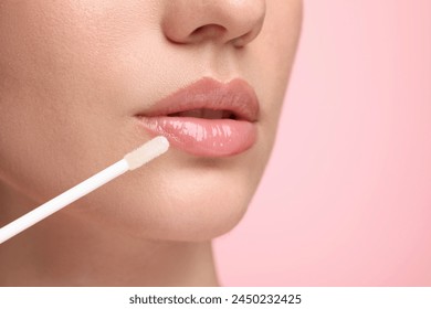 Woman applying lip gloss on pink background, closeup. Space for text - Powered by Shutterstock