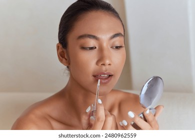 Woman Applying Lip Gloss While Looking In Hand Mirror Captures Cosmetics, Beauty Ritual, Femininity, Self-Care, And Makeup Routine. - Powered by Shutterstock