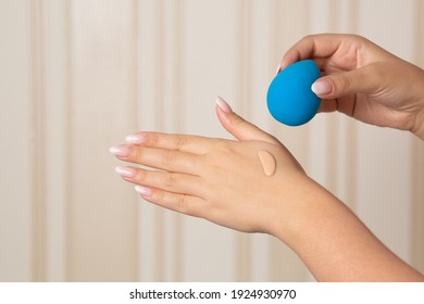 Woman applying liquid foundation with blue beauty blender from her hand. Space for text
