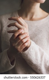 Woman applying moisturizing cream on hands. She wear roze sweater