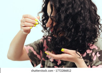 Woman applying natural oil on the tips of her curly hair, close up. Curly woman using serum for hair at home. Healthy curly hair. Natural products and cosmetics for hair.