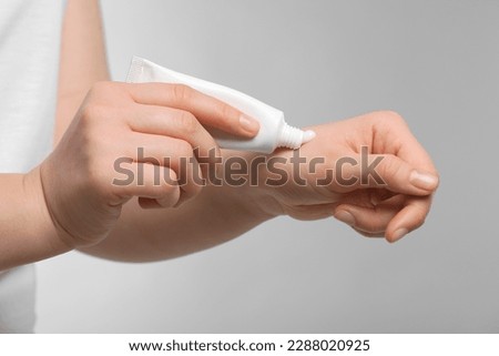 Woman applying ointment from tube onto her hand on light grey background, closeup
