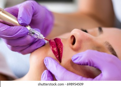 Woman applying permanent make up on lips in beautician salon with tattoo tool. Selective focus close up - Shutterstock ID 698954509