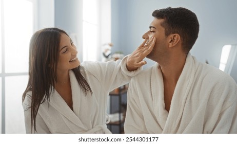 Woman applying skincare to man's face while wearing robes in a relaxing spa setting, highlighting their joyful relationship and serene wellness experience indoors - Powered by Shutterstock