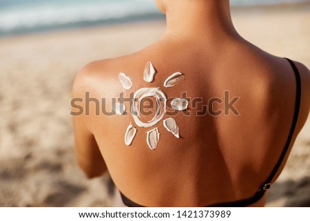 Woman Applying Sun Cream on Tanned  Shoulder In Form Of The Sun. Sun Protection.Sun Cream. Skin and Body Care. Girl Using Sunscreen to Skin. Female Holding Suntan Lotion and Moisturizing Sunblock.