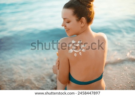 Woman Applying Sun Cream on Tanned Shoulder In Form Of The Sun. Sun Protection.Sun Cream. Skin and Body Care. Girl Using Sunscreen to Skin. Female Holding Suntan Lotion and Moisturizing Sunblock