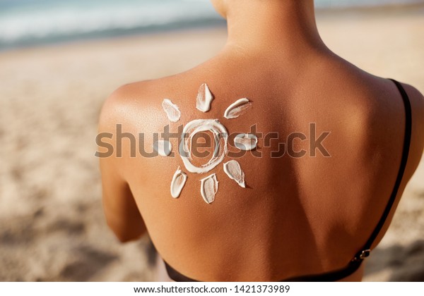 Woman Applying Sun Cream on Tanned  Shoulder In\
Form Of The Sun. Sun Protection.Sun Cream. Skin and Body Care. Girl\
Using Sunscreen to Skin. Female Holding Suntan Lotion and\
Moisturizing Sunblock.