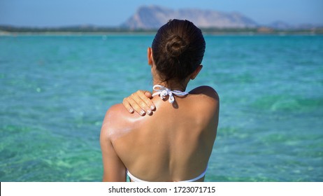 Woman applying sunscreen creme on tanned shoulder over the sea
