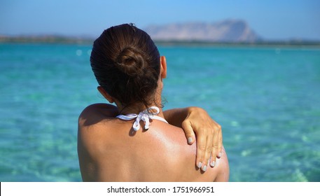 Woman applying sunscreen creme on tanned shoulder over the sea