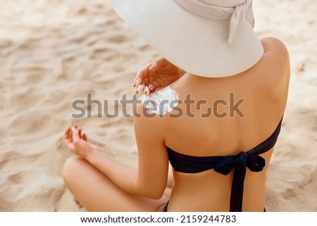 Woman applying sunscreen creme on  tanned  shoulder. Skin care. Body Sun protection sun cream. Bikini hat woman applying moisturizing sunscreen lotion on back.