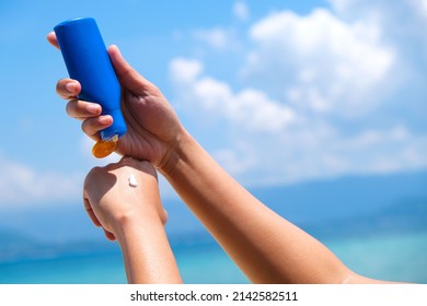 A woman is applying sunscreen and skin care to protect her skin from UV rays. She is applying sunscreen on her hand and arm. The sun symbol is a very sunny background. Health and skin care concept