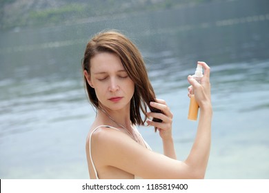 Woman applying sunscreen spray on the beach, hair care protection concept