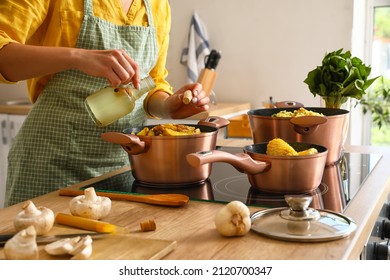 Woman in apron adding oil from bottle to cooking pot with vegetable stew in kitchen - Powered by Shutterstock