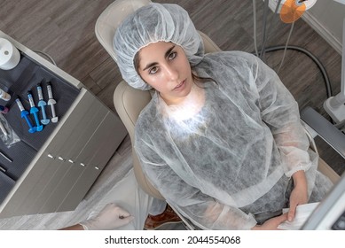 Woman With Apron And Disposable Cap Prepares To Be Seen By Her Dentist