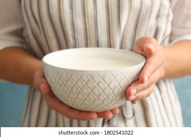 Woman in apron hold bowl of sour cream yogurt against blue background