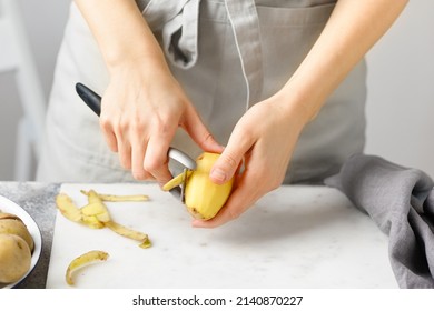 Woman in apron peeling potato on marble board. White background. Hands peeling potato with kitchen peeler. Food preparation - Powered by Shutterstock