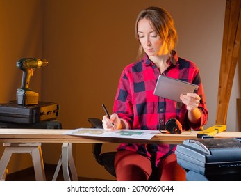 Woman Architect In Carpentry Workshop. Architect-designer At Work. Girl Furniture Maker Works With Drawings. Concept - Custom-made Wooden Furniture. Girl Architect Next To Construction Tools