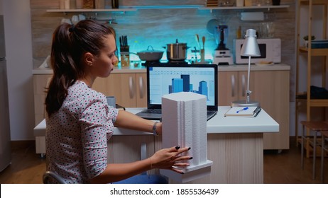 Woman Architect Matching Prototype With Plans From Laptop Working From Home Overtime. Designer Using Cad Software To Design A 3D Concept Of Buildings Creating And Studying Late At Night