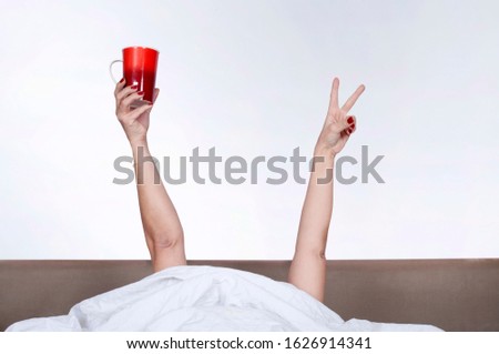 woman arm raised and holding cup of coffee in bed