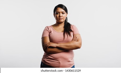 Woman With Arms Crossed Standing Against White Background. Portrait Of An Obese Woman Looking At Camera.