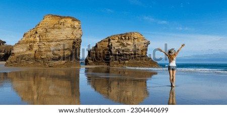 Woman with arms raised enjoying atlantic ocean and rock formation- cathedral beach with arch and cave- Galicia,  Spain