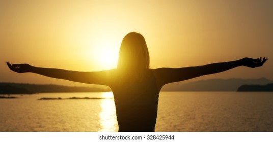 Woman with arms wide open at sunset.