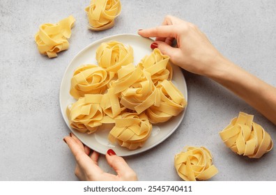 Woman arranging uncooked pasta nests on a white plate on a gray background, preparing a traditional italian meal - Powered by Shutterstock