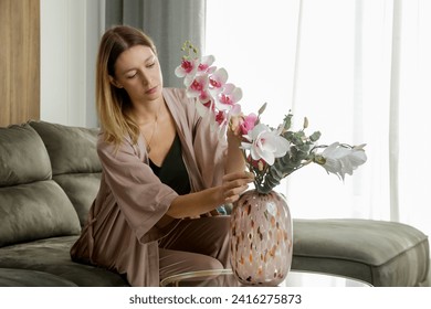 Woman arranging vase with flowers on dining table. Housewife taking care of coziness in apartment. Interior decor, household and home improvement concept.	 - Powered by Shutterstock