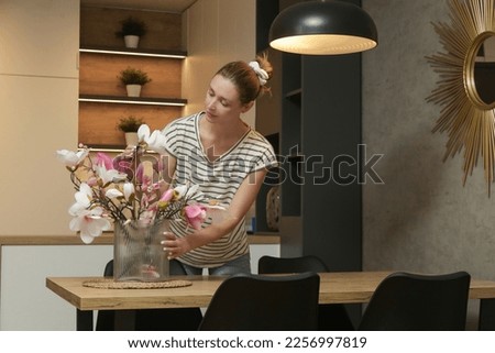 Woman arranging vase with flowers on table. Housewife taking care of coziness in apartment. Interior decor, household and home improvement concept.