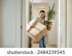 Woman arriving at her new house with her plant and a box with her belongings. Happy young girl carrying a plant and a moving box to her new house, to a student apartment or a flat for work transfer.