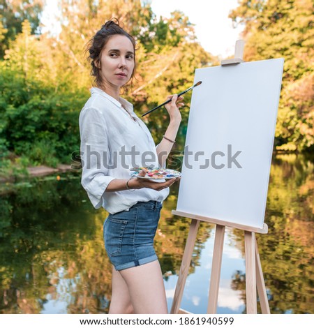 woman artist summer park lake, background forest water shore trees, draws picture, view from front, hand palette with paints, brush asel. Clothes white shirt shorts. White blank canvas, start drawing Stock photo © 