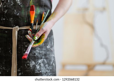 Woman artist's hand with a brush and red paint. Black apron, white background in the art studio. Copy space. - Powered by Shutterstock