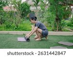 A woman of Asian descent prepares for her yoga session by rolling out a mat in a lush garden filled with greenery, surrounded by vibrant plants in the early morning light.