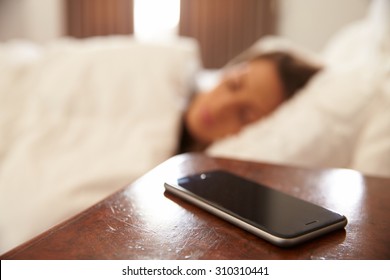 Woman Asleep In Bed With Mobile Phone On Bedside Table