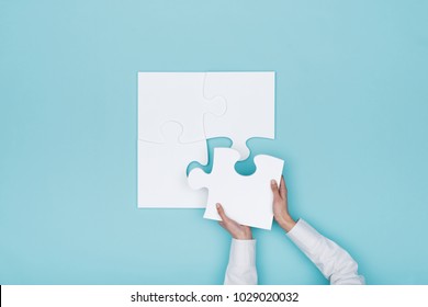 Woman assembling a jigsaw puzzle she is adding the last missing piece, solutions and challenges concept - Shutterstock ID 1029020032