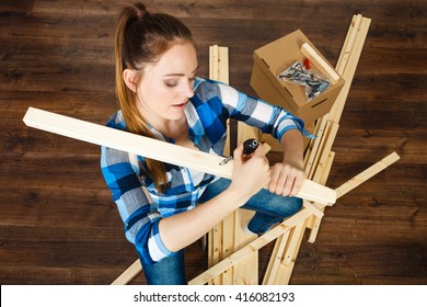 Woman Assembling Wooden Furniture Using Screwdriver. DIY Enthusiast. Young Girl Doing Home Improvement.