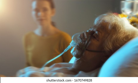 Woman Assisting An Elderly Patient With Oxygen Mask At Night, Senior Care Concept