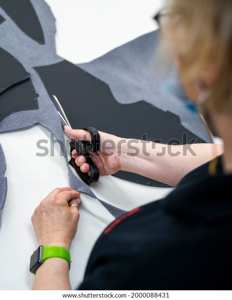 a woman in an atelier\
cuts leather elements with scissors for covering an expensive car\
interior