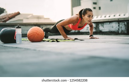 Woman athlete doing push ups on the rooftop with medicine ball and basketball by her side. Woman in fitness wear doing workout on the terrace. - Powered by Shutterstock