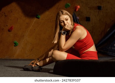 Woman athlete looks bored sitting on mat before workout. Lady waits for bouldering session with instructor at indoor climbing gym - Powered by Shutterstock