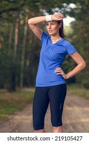 Woman Athlete Wiping Sweat From Her Forehead Onto Her Wristband As She Pauses During Her Training Exercises On A Forest Track