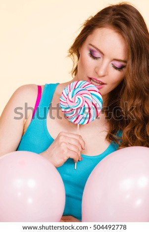 Woman attractive cheerful girl holding colorful balloons and sweet lollipop in hands. Summer holidays, celebration and happiness concept. Studio shot bright yellow background