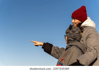 A woman in an autumn jacket and her child are walking on a deserted autumn beach on a sunny day and looking at something in the distance with their hand. Family relations. Motherhood. healthy lifest