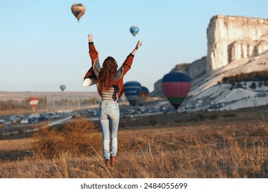 Woman in awe of colorful hot air balloons soaring in the sky on a sunny day - Powered by Shutterstock